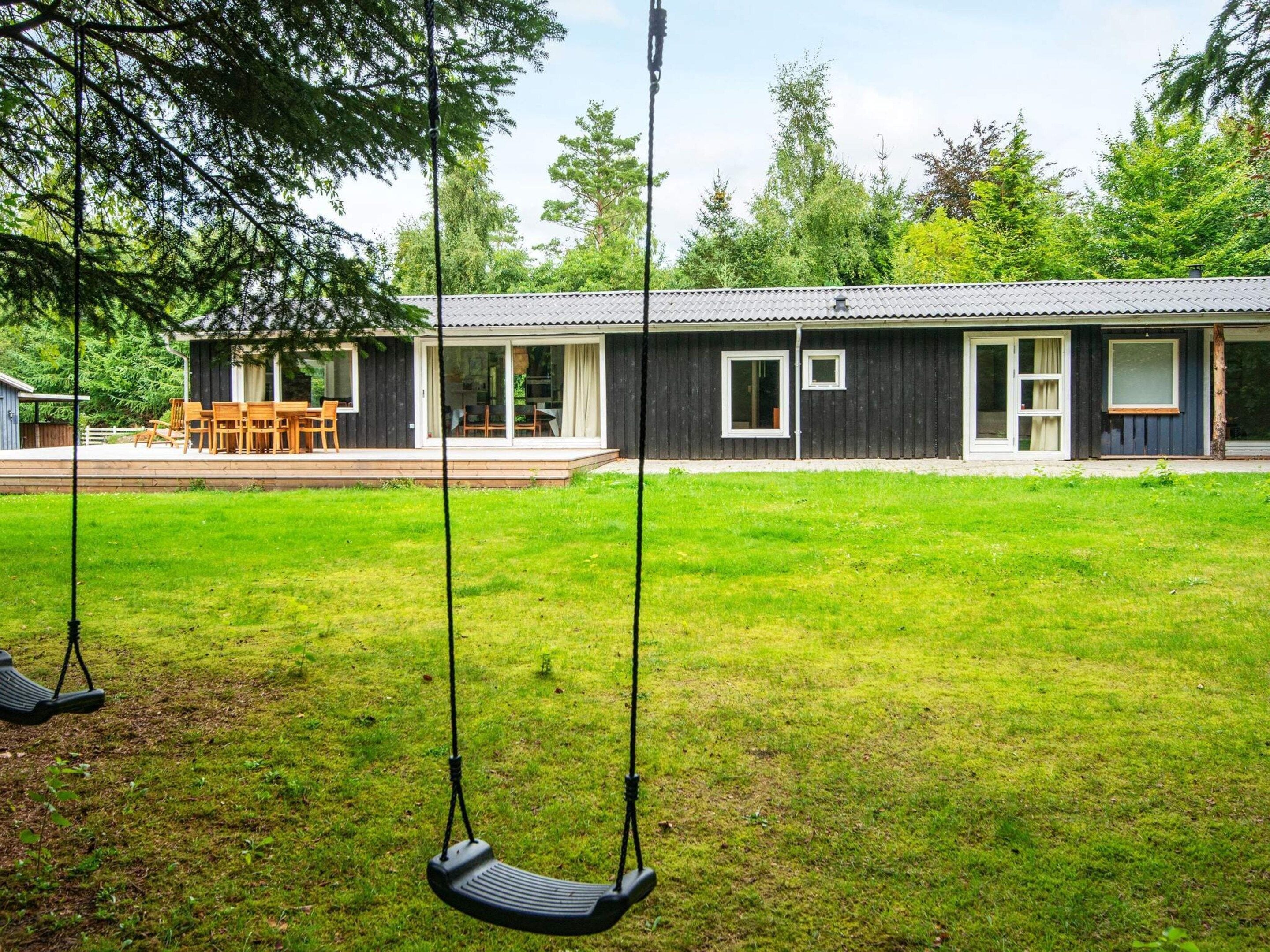 A house with a covered patio, a swing set, and a lawn.