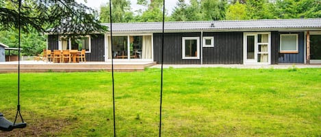 A house with a covered patio, a swing set, and a lawn.