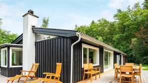 Ett modernt hus med en veranda, trämöbler och en skorsten.