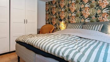 Un dormitorio con cama, una silla, armario y papel tapiz floral.