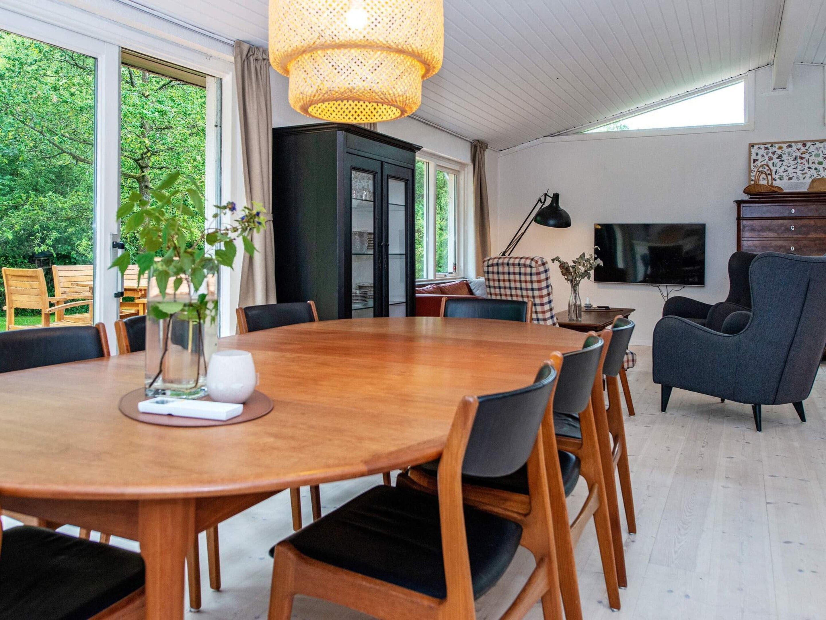A dining area with a round wooden table, chairs, a vase with flowers, and a television on the wall.