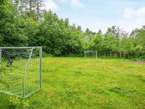 Un campo de fútbol con dos porterías y una valla de malla, rodeado de árboles y césped.
