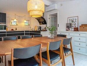 Eine moderne Küche mit Essbereich, ausgestattet mit einem Holztisch und -stühlen, einer Hängeleuchte und einem weißen Schrank mit Schubladen.