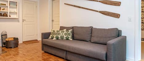 Una habitación con un sofá gris, suelo de madera y dos palas de madera en la pared.