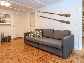 A room with a grey sofa, wooden flooring, and two wooden paddles on the wall.