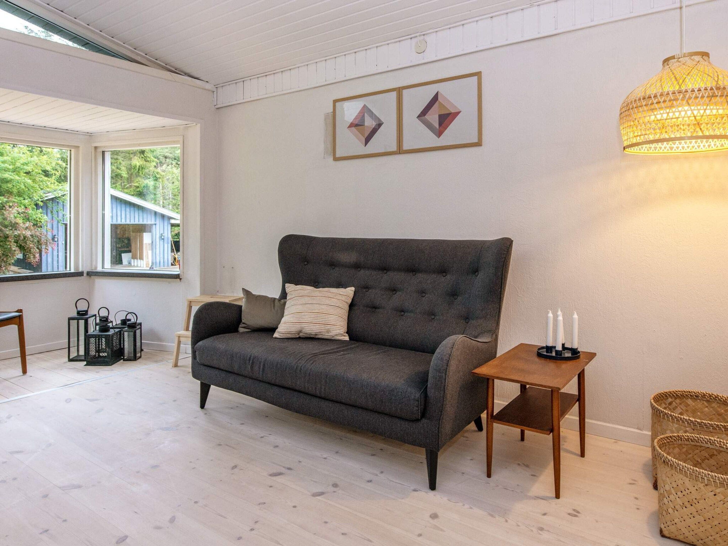 A cozy living room with a dark grey sofa, a small wooden side table with candles, and a woven basket.