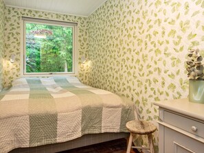 Une chambre à coucher avec un lit, une fenêtre, une commode et un tabouret.
