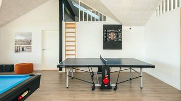 Ein geräumiges Zimmer mit einer Tischtennisplatte, einer Billardkugel und einer Dartscheibe an der Wand.
