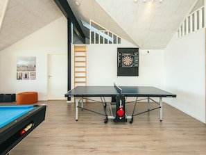 A spacious room with a ping pong table, a pool table, and a dartboard on the wall.
