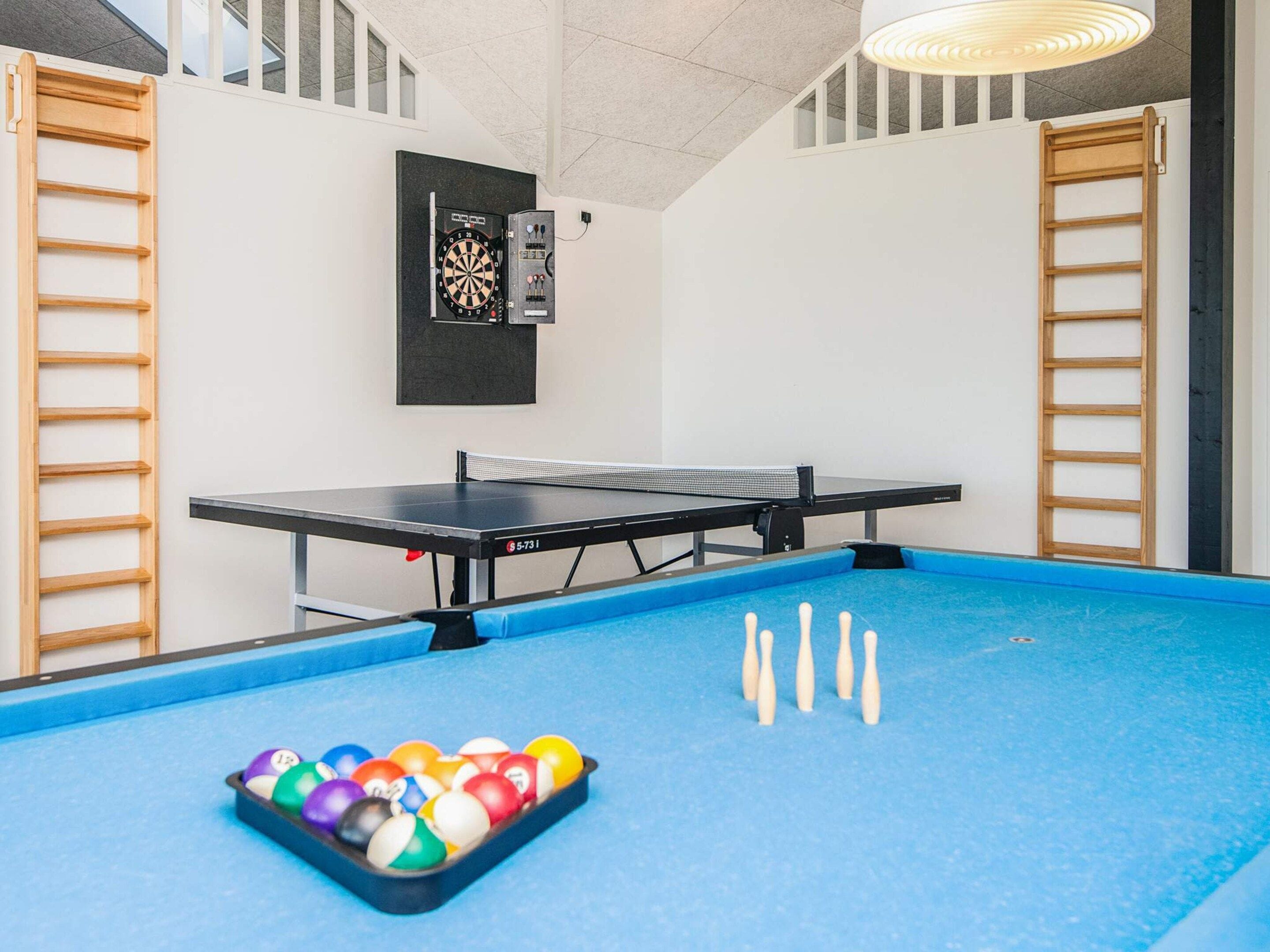 A billiards table with a rack of billiard balls, a dartboard, and two wooden ladders against the walls.