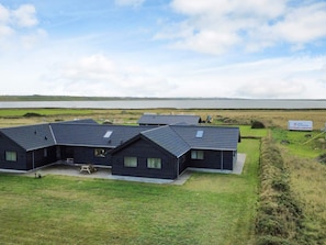 A row of dark-colored cabins with a grassy yard and a view of a body of water. - 5 Star Holiday Home in Harboore (Harboore)