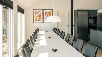 Ein Konferenzraum mit langem Tisch, Stühlen, einer weißen Pendelleuchte und zwei gerahmten Kunstwerken an der Wand.