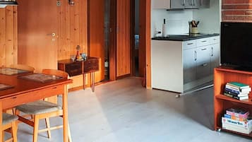 Un interior moderno con una mesa de comedor de madera, sillas, una zona de cocina con armarios y una televisión, además de una estantería.