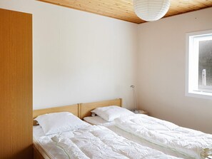 A bedroom with a wooden ceiling, a single bed with white bedding, a bedside table, and a window with blinds.