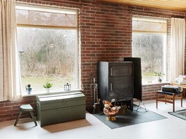 Una habitación con chimenea, un aparador verde, un taburete pequeño y una ventana con vista a árboles.