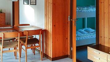 Una habitación con escritorio de madera, sillas, una cama litera y una puerta que da a otra habitación.