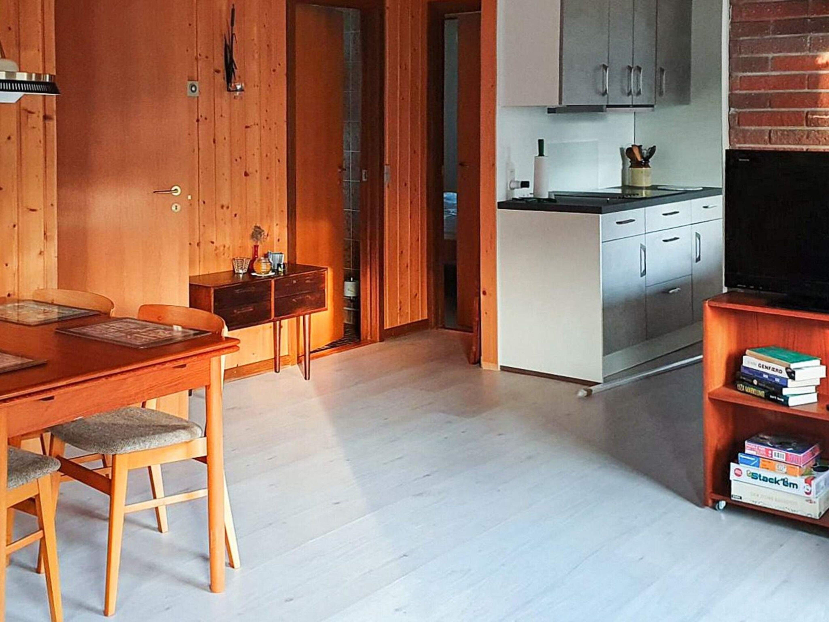 A compact living space with a wooden dining table, chairs, a kitchenette, and a television.