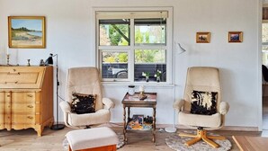 A cozy room with two armchairs, a wooden dresser, and a small table with a lamp. A window provides a view of greenery outside. - 7 Person Holiday Home in Hojslev (Hojslev)