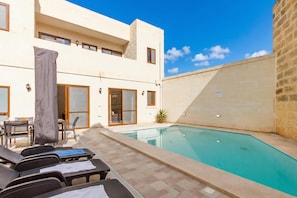 A poolside area with lounge chairs, a covered seating area, and a building with a tiled exterior.