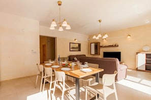 A dining area with a wooden table set for six, white chairs, and a brown sofa in the background.