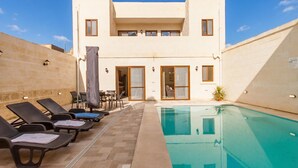 A poolside area with lounge chairs, a pool, and a building with a flat roof and large windows.