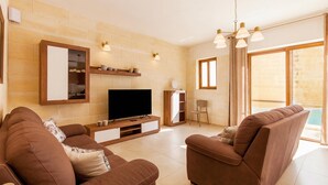 A living room with a TV, sofas, a coffee table, and a large window with curtains.