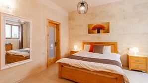 A bedroom with a wooden bed, a nightstand with a lamp, a mirror, and a painting on the wall.