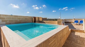Ein Dachpool mit Whirlpool, Holzterrasse und blauen Liegestühlen.