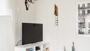 A modern living room with a flat-screen TV on a white stand, a mounted deer antler, a wall-mounted wooden sculpture, and a framed cityscape photo. - Tranquil Retreat by the Sea - By Traum Ferienwohnungen (Slagelse)