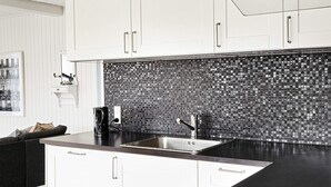 A modern kitchen with white cabinets, a black countertop, and a backsplash with a mosaic tile pattern. - Tranquil Retreat by the Sea - By Traum Ferienwohnungen (Slagelse)