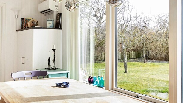 A dining area with a table, chairs, and hanging pendant lights. There is a window with a view of a garden. - Tranquil Retreat by the Sea - By Traum Ferienwohnungen (Slagelse)
