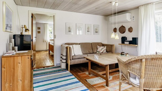 Un salon chaleureux avec un canapé, une table basse, un fauteuil en osier et un téléviseur posé sur un meuble en bois.