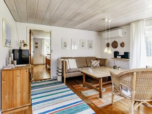 Ein gemütliches Wohnzimmer mit einer Couch, einem Couchtisch, einem Korbstuhl und einem Fernseher auf einem Holzschrank.