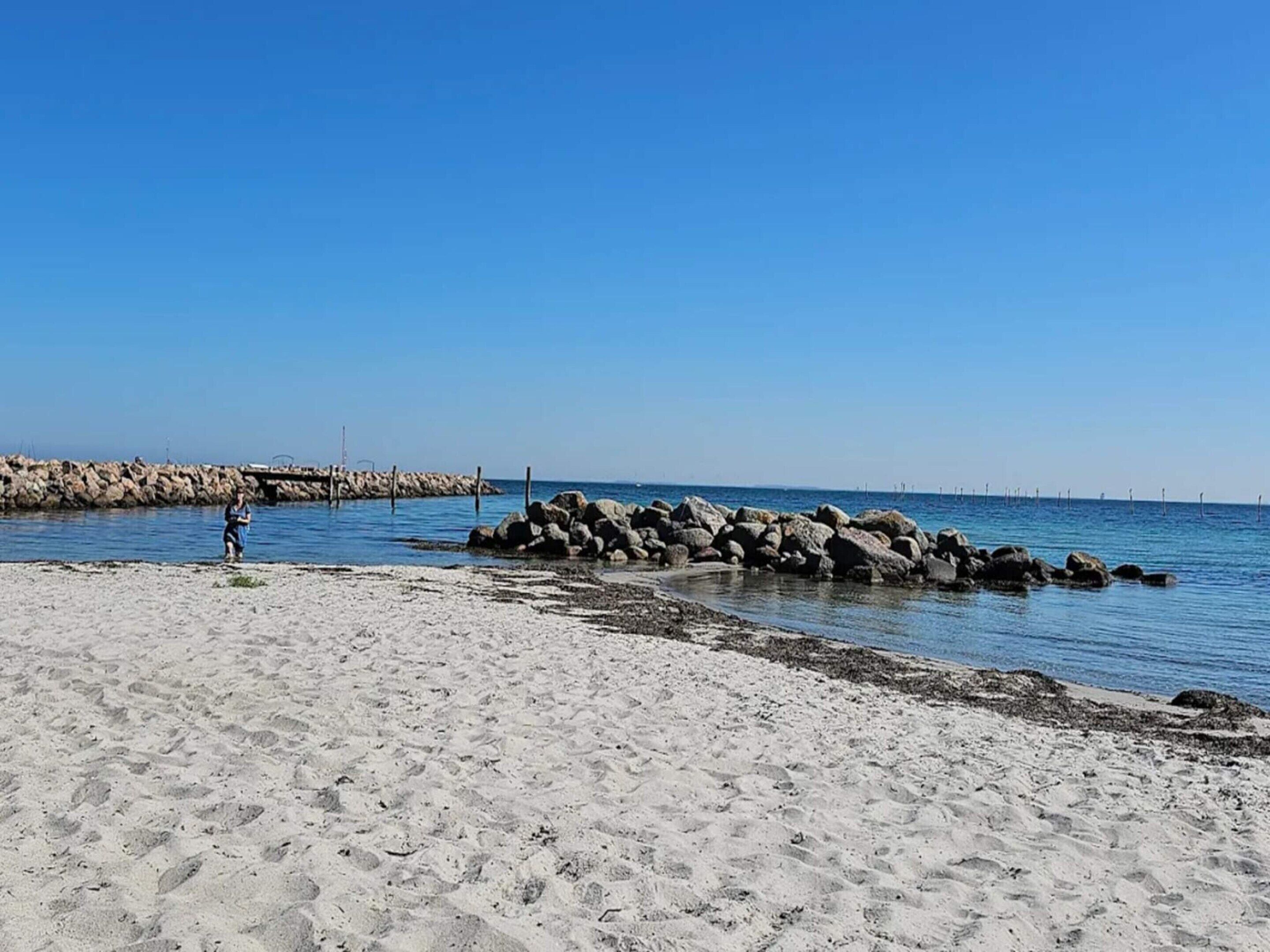 A sandy beach with a rocky breakwater and calm water.