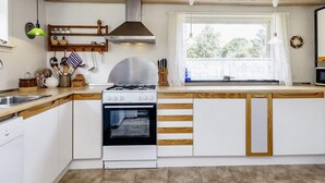 Une cuisine moderne avec des meubles blancs, une hotte en acier inoxydable et une fenêtre agrémentée de rideaux.