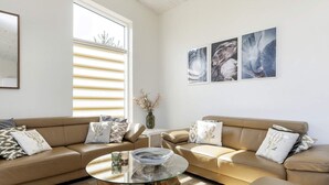 A modern living room with a beige leather sofa, a glass coffee table, and a wooden side table. There are three framed artworks on the wall and a vase with dried flowers on a small table. - 10 Person Holiday Home in Vaeggerlose (Vaeggerlose)