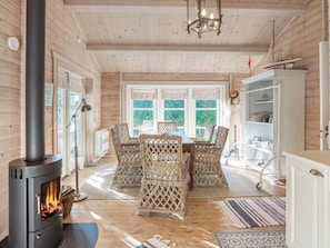 A cozy wooden interior with a central fireplace, wicker furniture, and a view through large windows. - 6 Person Holiday Home in Vaeggerlose (Vaeggerlose)