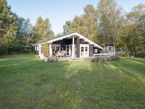 A two-story house with a covered porch, a lawn, and trees in the background. - 6 Person Holiday Home in Vaeggerlose (Vaeggerlose)