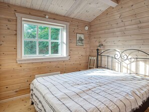 Een kamer met houten wanden, een bed met metalen frame, een raam met uitzicht op groen en een kleine tafel.