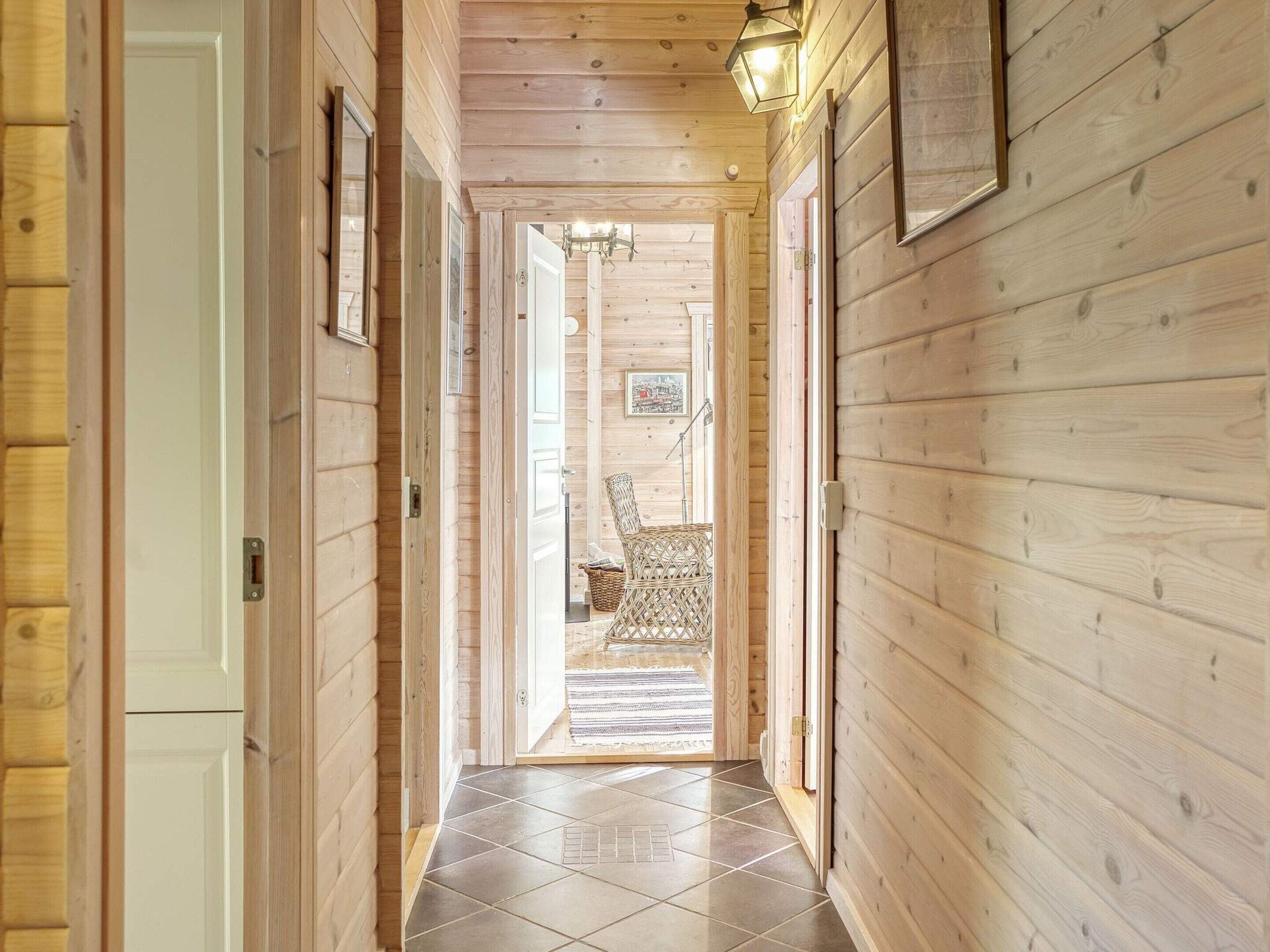 A wooden interior hallway with a tiled floor, a wicker chair, and a framed picture on the wall.