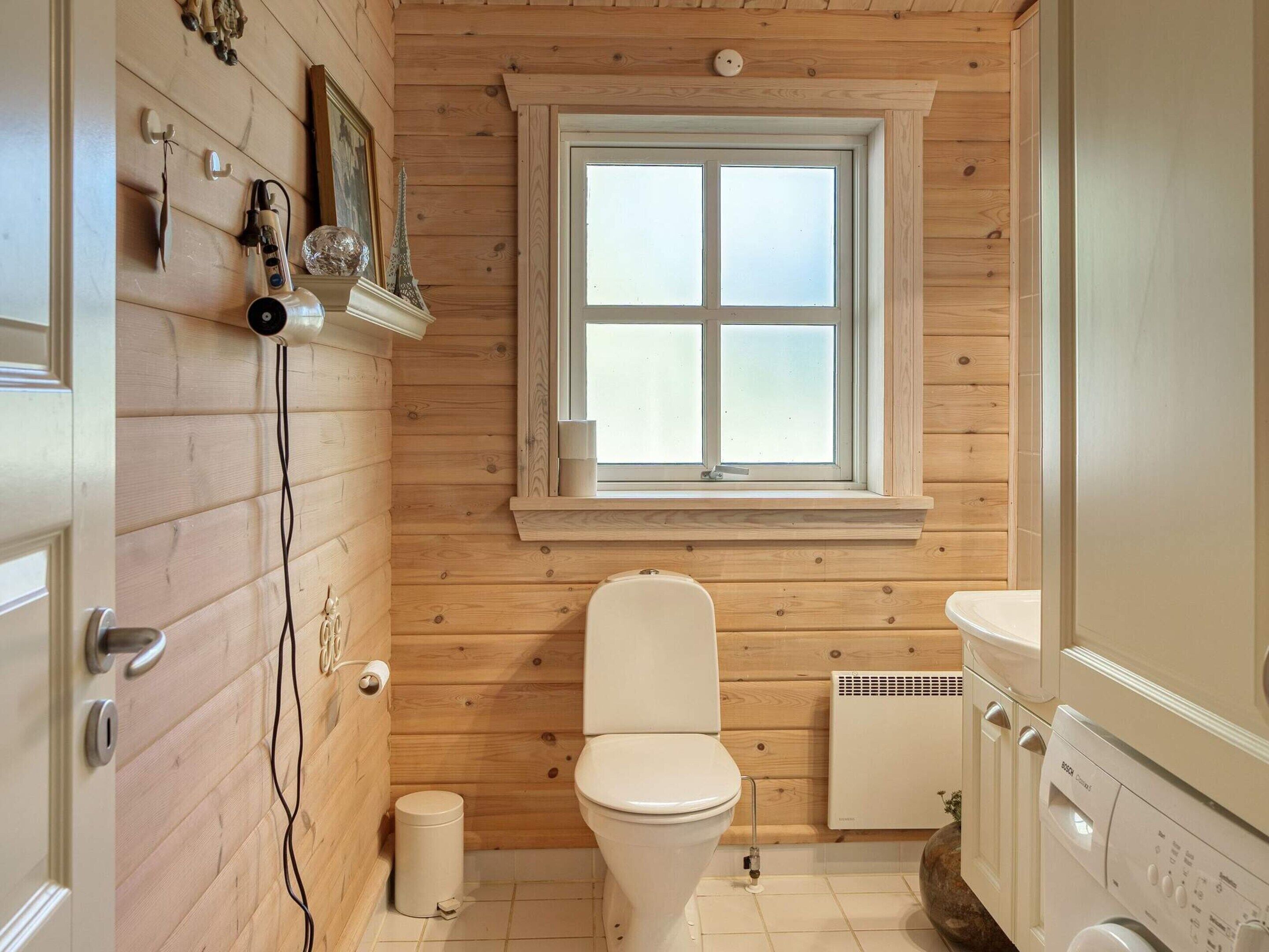 Un baño con paneles de madera, un inodoro, una ventana y una lavadora.