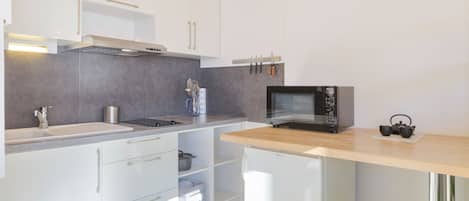Una cocina moderna con armarios blancos, un lavamanos de acero inoxidable, un microondas y una encimera de madera.