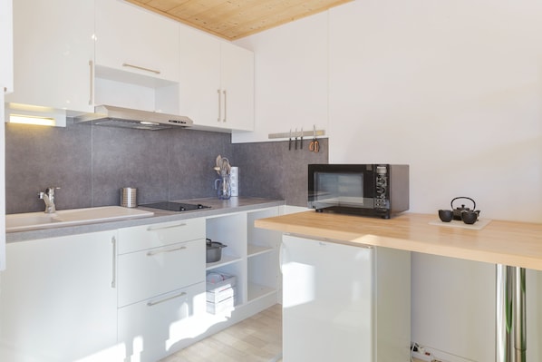 Une cuisine moderne avec des meubles blancs, un évier en acier inoxydable, un four à micro-ondes et un plan de travail en bois.