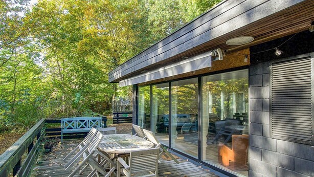A modern outdoor deck with a glass-enclosed patio area, wooden deck, and outdoor furniture.