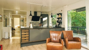 A modern kitchen with a central island, two leather chairs, and a large window overlooking greenery.