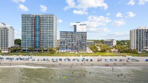 A beachfront hotel with multiple high-rise buildings, a sandy beach with umbrellas, and ocean views. - Romantic Oceanfront Condo w/ Beach Access, King Bed, Onsite Bar & Restaurant! (Myrtle Beach)