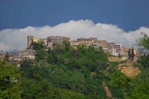 A historic town with buildings on a hillside, surrounded by dense greenery and a partly cloudy sky.