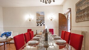 Comedor con mesa de vidrio dispuesta para una comida, sillas tapizadas en rojo y un candelabro.