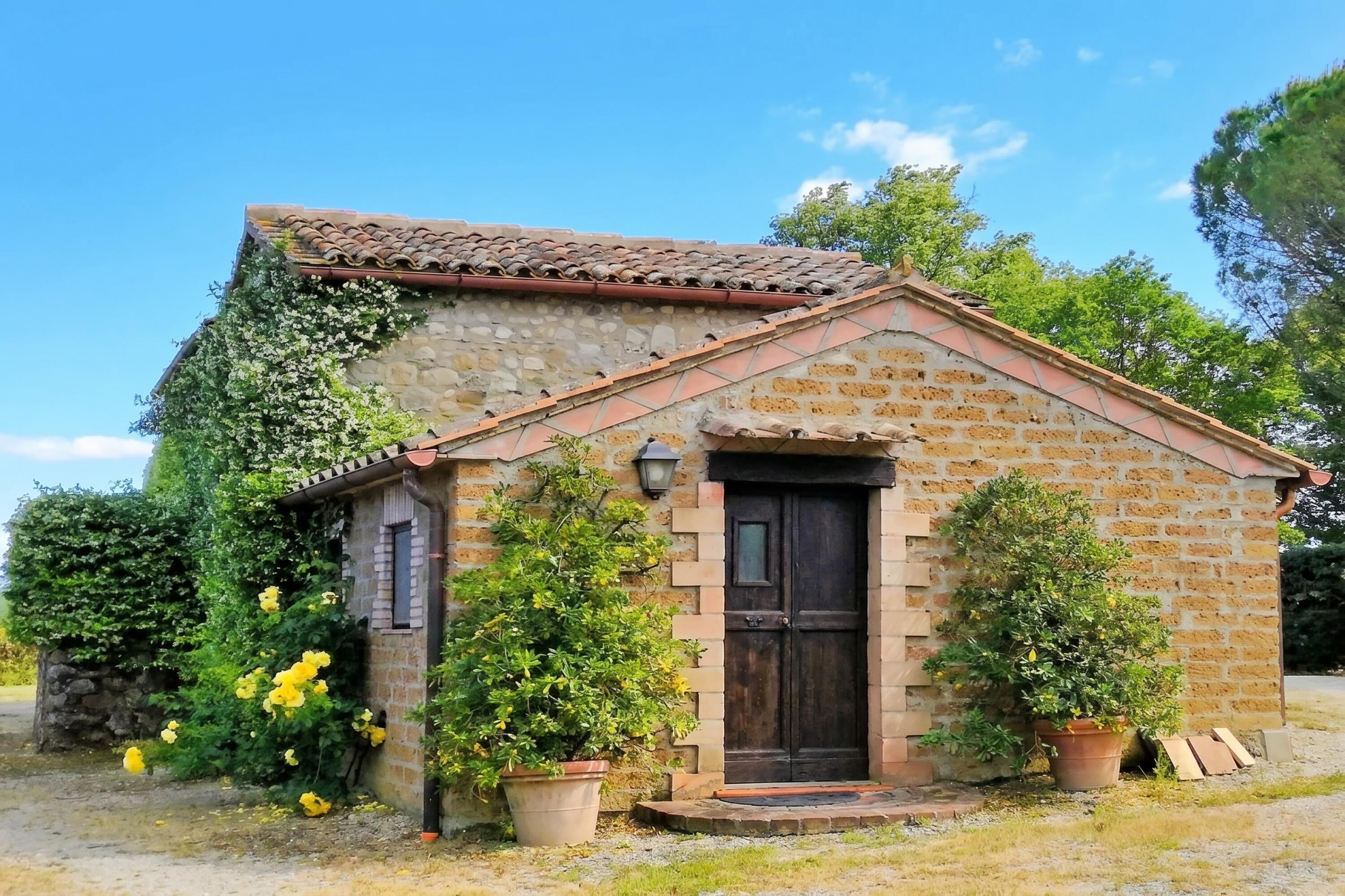 A small stone building with a tiled roof, a dark wooden door, and potted plants.