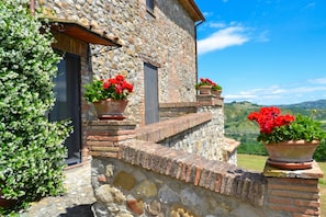 A stone building with a stone staircase, potted red flowers, and a view of green hills.